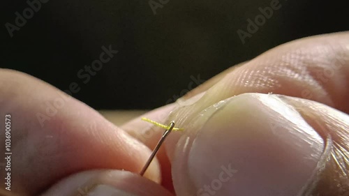 Close up view of a man's hand inserting a yellow thread through eye of needle