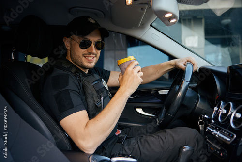 Portrait of smiling patrolman driving car drinking takeaway coffee