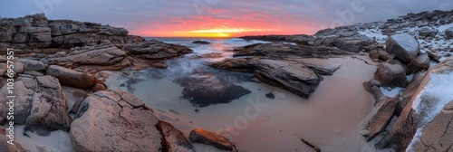 rocks and snow-covered ground precede a tranquil water foreground, as the sun sets over a rocky beach photo