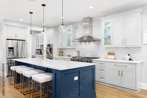 A kitchen with blue and grey cabinets, a large island with gold and white bar stools sitting at the white marble countertop, subway tile backsplash, and gold faucet and hardware. No brands or labels.