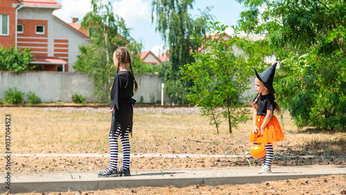 Children wearing black and orange witch costumes with hats playing in autumn Park on Halloween. Kids trick or treat.