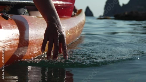 Kayaking Hand Water - A hand reaches into the water from a kayak near a rocky shore. photo