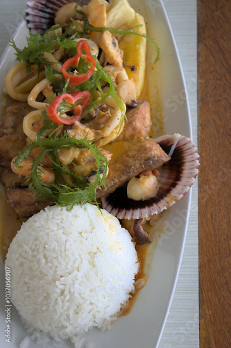 A vertical view of a Peruvian dish Pescado a lo Macho with seafood and white rice.