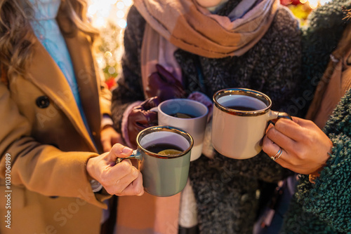 Friends holding mugs of hot drinks at Christmas market, winter fashion, festive atmosphere