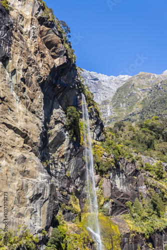 Waterfall cascading down rocky cliff in milford sound fiordland new zealand