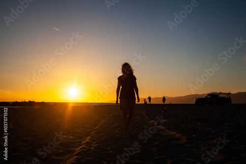 Woman walking on the beach at sunset with people in the distance