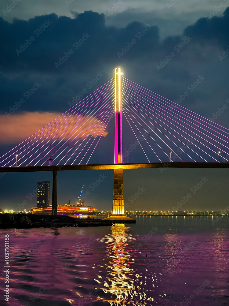 Fototapeta premium Cebu City, Philippines - CCLEX bridge illuminated at night, reflecting vibrant colors over the water.