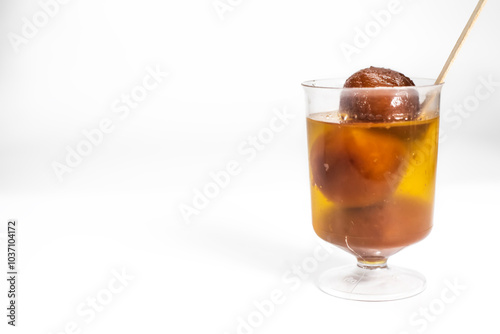 Gulab jamun in sugar syrup in a transparent glass cup with a wooden spoon