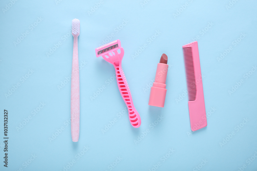 Personal hygiene items. Pink Toothbrush with razor and comb, lipstick on blue background. Top view Personal hygiene items. Pink Toothbrush with razor and comb, lipstick on blue background. Top view
