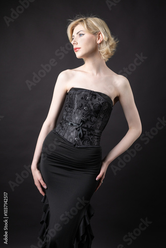 Expressive young blonde under a bob in the studio. In a black corset and dress.