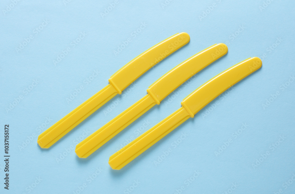 Obraz premium Yellow Plastic knives on blue background