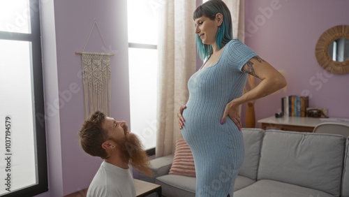 Pregnant woman and man in a beautiful indoor home setting, capturing a loving moment together as the man kneels, looking adoringly at her baby belly. photo