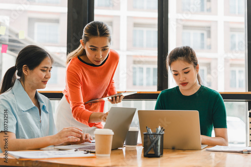 Collaborative meeting with three women working together in modern office. They are engaged in discussion, sharing ideas, and using laptops. atmosphere is focused and productive