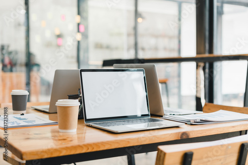 modern workspace featuring laptops, coffee cups, and documents on wooden table. clean and organized setup promotes productivity and creativity in contemporary office setting