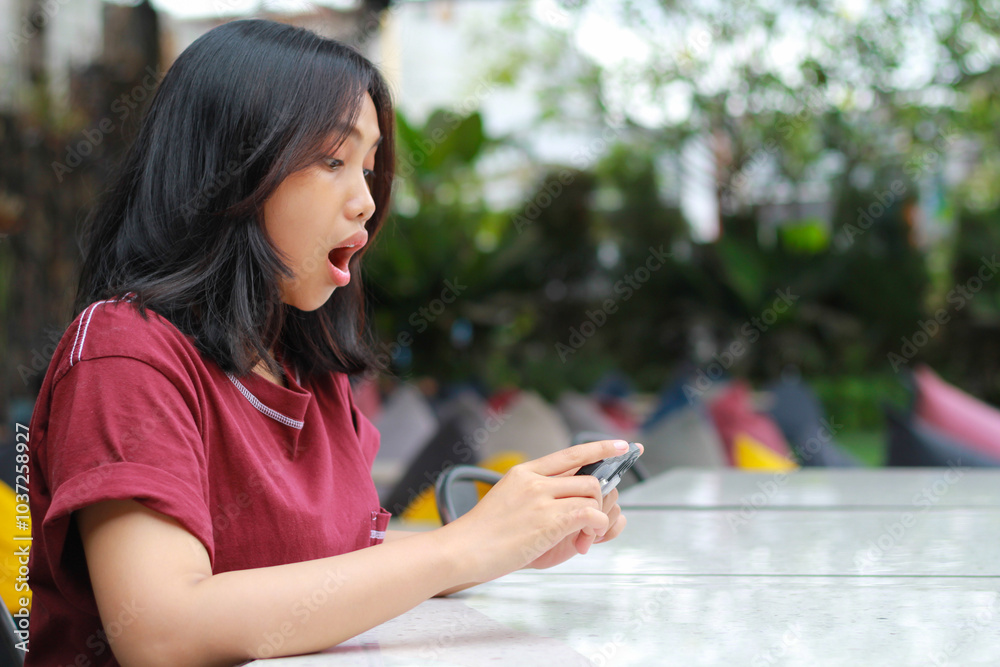 pretty asian woman amazed playing online game using smartphone while sitting in cafe pretty asian woman amazed playing online game using smartphone while sitting in cafe