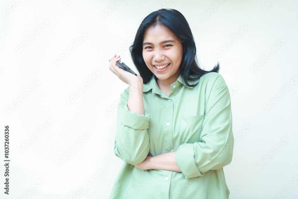 carefree asian woman with dark hair wearing green over size shirt enjoy talking on smartphone with arms folded, playful stylish female looking at camera, standing over isolated white background carefree asian woman with dark hair wearing green over size shirt enjoy talking on smartphone with arms folded, playful stylish female looking at camera, standing over isolated white background