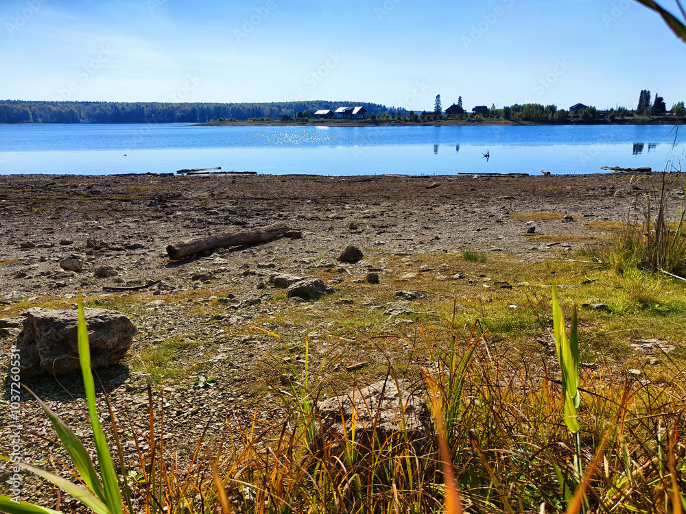 Tranquil lakeside view with grassy hillside under a clear blue sky in the afternoon