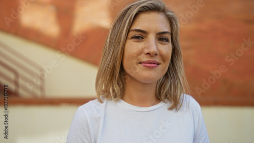 Young, attractive, blonde, woman standing on an urban street with a brick wall background on a sunny day