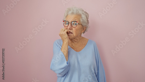 Canvas Print A surprised elderly woman with grey hair, wearing glasses and a blue sweater, against a pink background