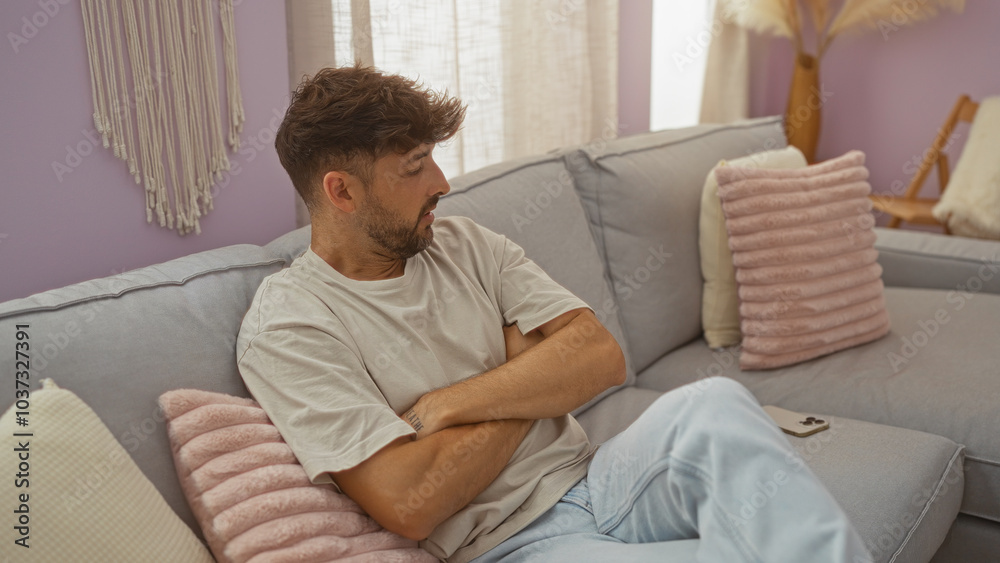 Young man with arms crossed sitting on a couch in a cozy living room with pastel colors and soft cushions. Young man with arms crossed sitting on a couch in a cozy living room with pastel colors and soft cushions.