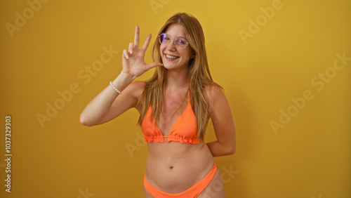 Young woman in orange bikini showing number three with fingers against isolated yellow background