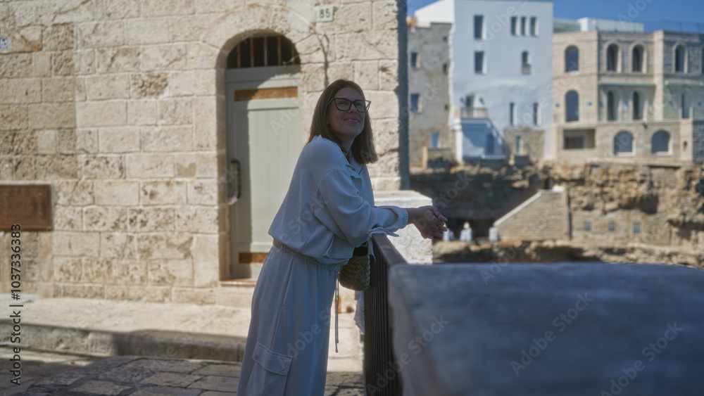 Woman enjoying the view from a balcony in polignano a mare, puglia, italy, europe, with historic stone buildings in the background on a sunny day. Woman enjoying the view from a balcony in polignano a mare, puglia, italy, europe, with historic stone buildings in the background on a sunny day.