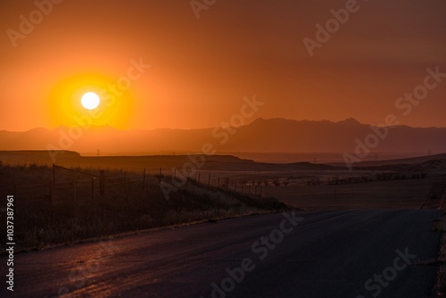 HDR Sunset layers of mountains in the background orange clouds beautiful rolling hills farm in Wyoming and bright sun on country road