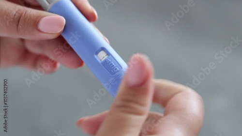 A super close up of a young woman priming the pen injector, prepering it for injection
