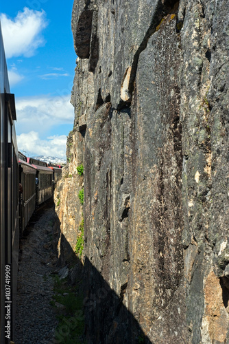 Passenger train out of Skagway runs next to sheer rock cliffs after crossing into Canada at the top of Alaska's White Pass.