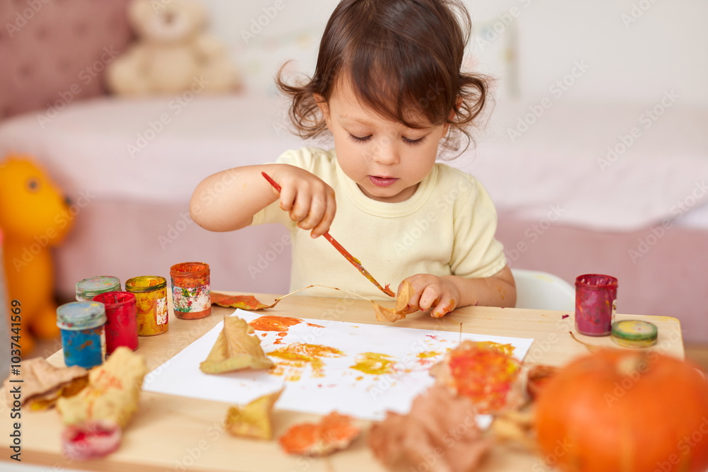 cute little child girl painting autumn leaves. baby girl drawing leaves in yellow and orange paint cute little child girl painting autumn leaves. baby girl drawing leaves in yellow and orange paint