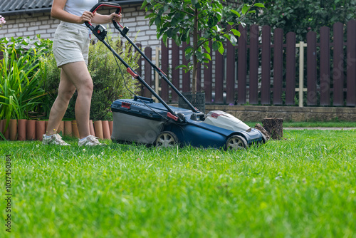 This image captures someone mowing their lawn with a push lawn mower. The person is holding onto the handle, guiding the mower over a well-maintained grassy area.