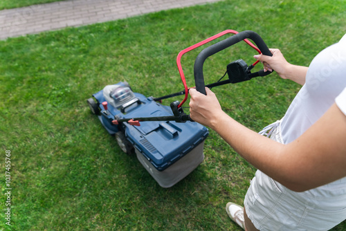 This image captures someone mowing their lawn with a push lawn mower. The person is holding onto the handle, guiding the mower over a well-maintained grassy area.