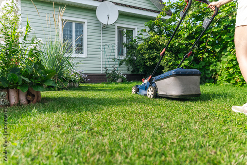 A lawn mower is cutting green grass, the gardener with a lawn mower is working in the backyard, a side view. photo