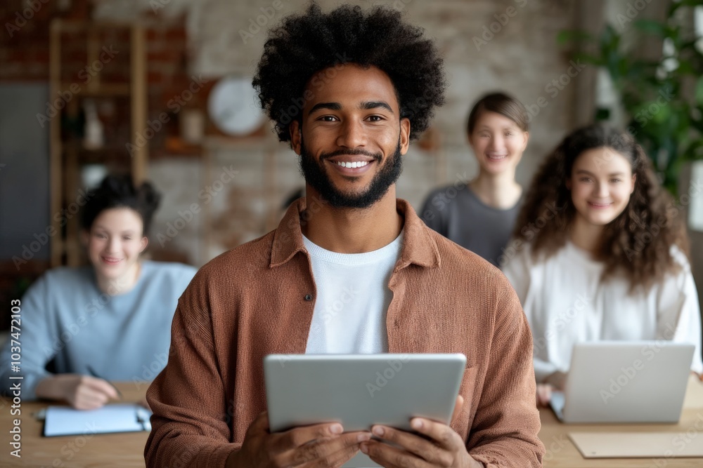 A man with a full beard and warm smile holds a tablet device, surrounded by diverse colleagues sitting at desks, symbolizing teamwork and diversity in the workplace. A man with a full beard and warm smile holds a tablet device, surrounded by diverse colleagues sitting at desks, symbolizing teamwork and diversity in the workplace.