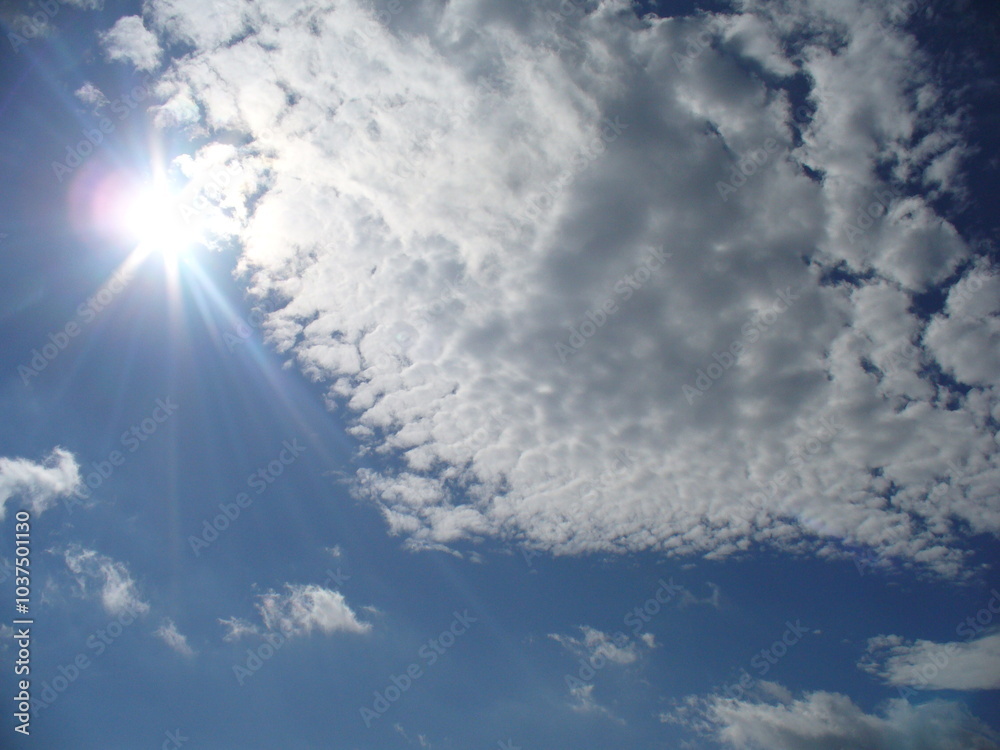 Optimistic, sunny blue sky with sun rays and white and grey clouds - natural background. Topics: weather, meteorology, sun energy, atmosphere, air space, season Optimistic, sunny blue sky with sun rays and white and grey clouds - natural background. Topics: weather, meteorology, sun energy, atmosphere, air space, season