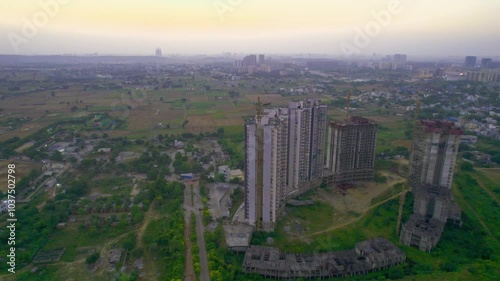 Aerial drone shot flying towards under construction building with crane on top surrounded by green fields showing the rapid development of skyscrapers multi-storey apartments office shopping malls photo