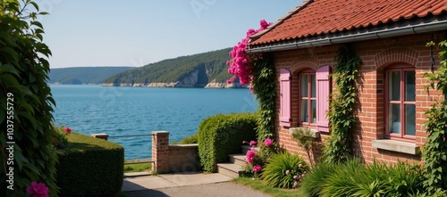 A red-roofed house sits amidst pink flowers overlooking tranquil waters photo