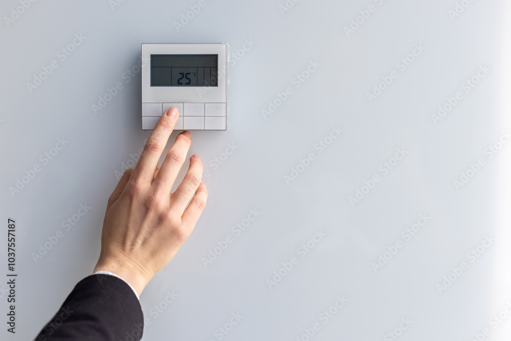 Close-up of hand adjusting digital thermostat set to 25 degrees Celsius. Concept of energy efficiency, climate control, and modern technology in home or office environment. Close-up of hand adjusting digital thermostat set to 25 degrees Celsius. Concept of energy efficiency, climate control, and modern technology in home or office environment.