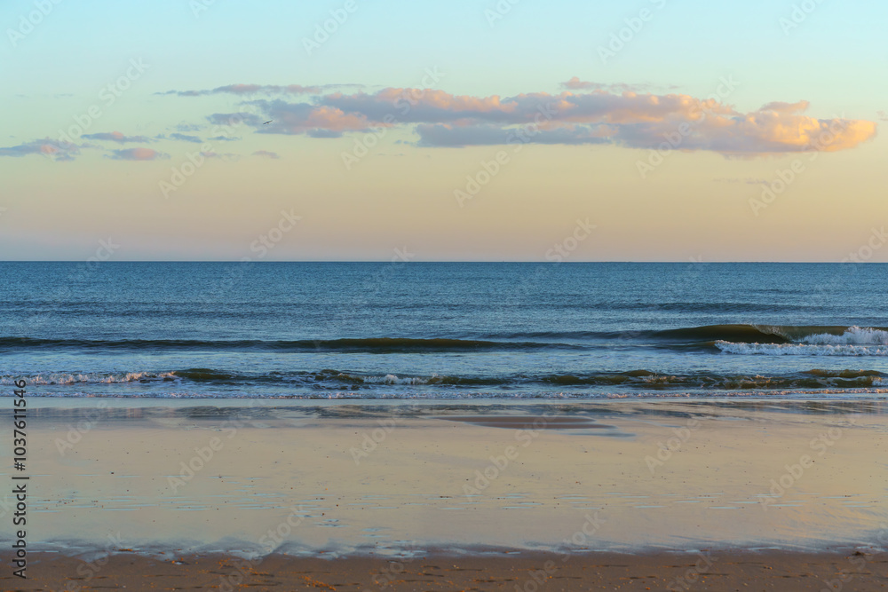 Calm ocean waves gently reaching the sandy shore under a soft pastel sky. Calm ocean waves gently reaching the sandy shore under a soft pastel sky.