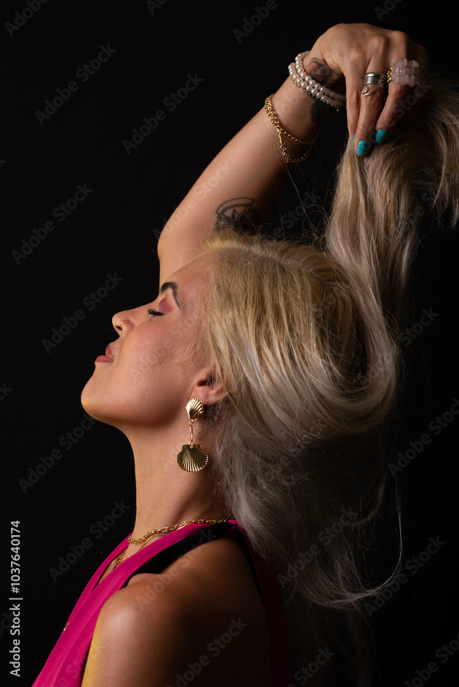 Fototapeta premium Beautiful Caucasian woman in red dress posing and touching her blonde hair. Isolated on black background. Salvador, Bahia.