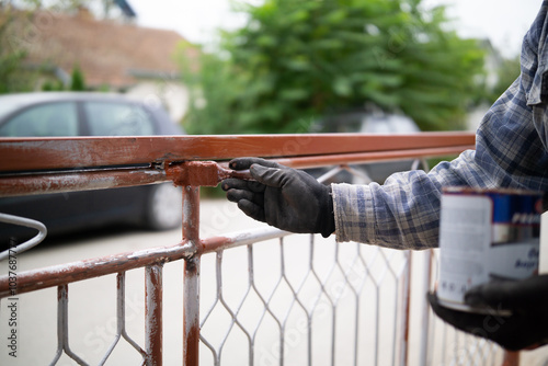 Male hand painting metal fence with a brush with red oxide metal primer