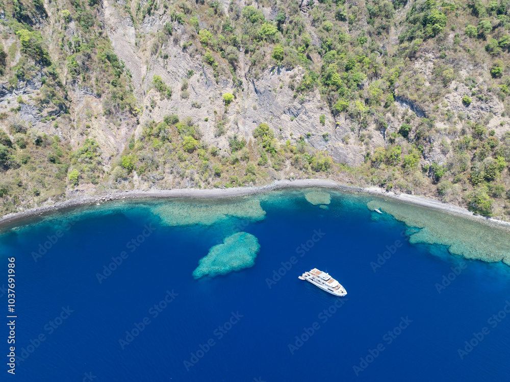 Obraz premium The scenic and rugged coastline of the island of Komba lies 70 km north of the Lesser Sunda Islands of Indonesia. This remote island, surrounded by reef, is an active volcano that often erupts.
