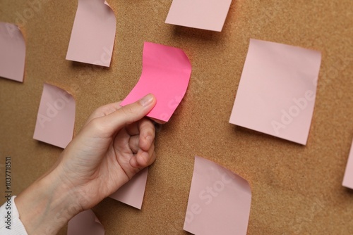 Woman taking empty paper note from cork board, closeup photo