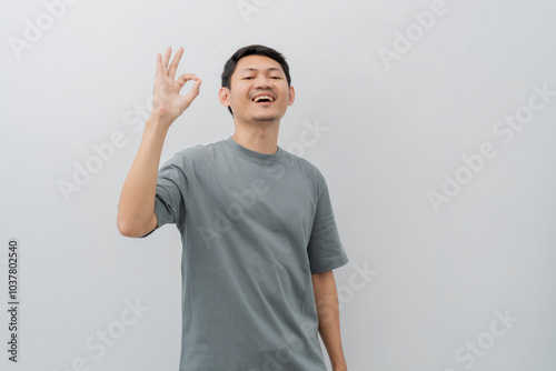 Happy expression of adult Asian man doing OK sign with casual t-shirt isolated on white background photo