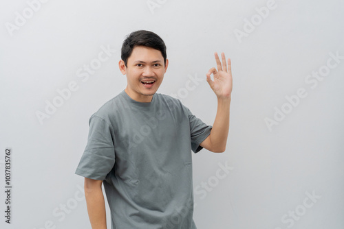 Happy expression of adult Asian man doing OK sign with casual t-shirt isolated on white background photo