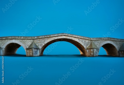An old stone bridge with three arches against a bright blue sky.