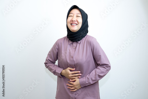 Portrait of emotional Indonesian woman laughing and wearing a purple shirt and black headscarf is laughing while pointing with her hands. isolated on white background