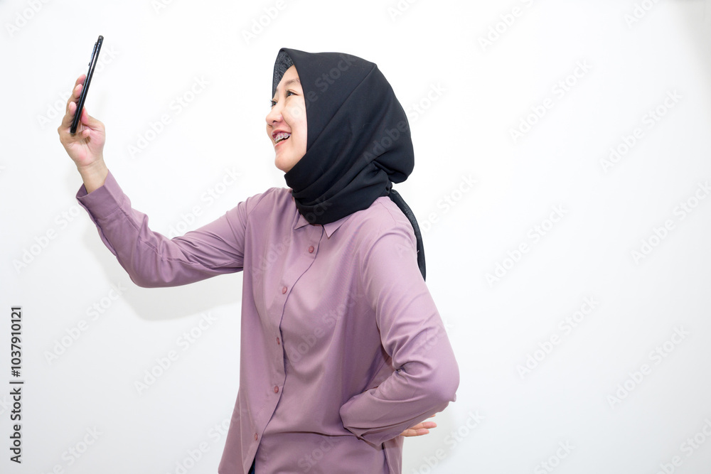 Portrait of emotional Asian, Indonesian woman wearing purple shirt and hijab headscarf laughing and holding handphone. Isolated on white background Portrait of emotional Asian, Indonesian woman wearing purple shirt and hijab headscarf laughing and holding handphone. Isolated on white background