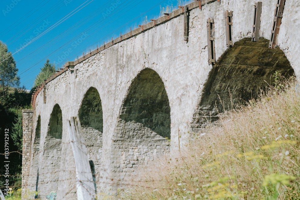 Historic stone viaduct with multiple arches surrounded by greenery under a clear blue sky Historic stone viaduct with multiple arches surrounded by greenery under a clear blue sky