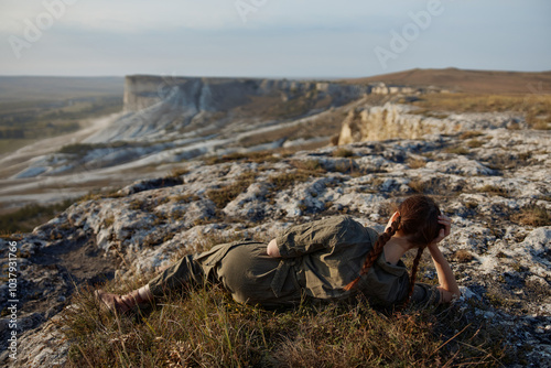 Woman relaxing on rock in tranquil field with majestic mountains in background in travel adventure scene photo